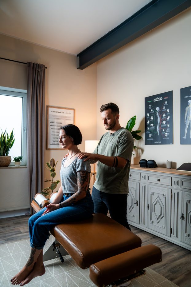 Behandlungssituation mit anatomischem Poster im Hintergrund